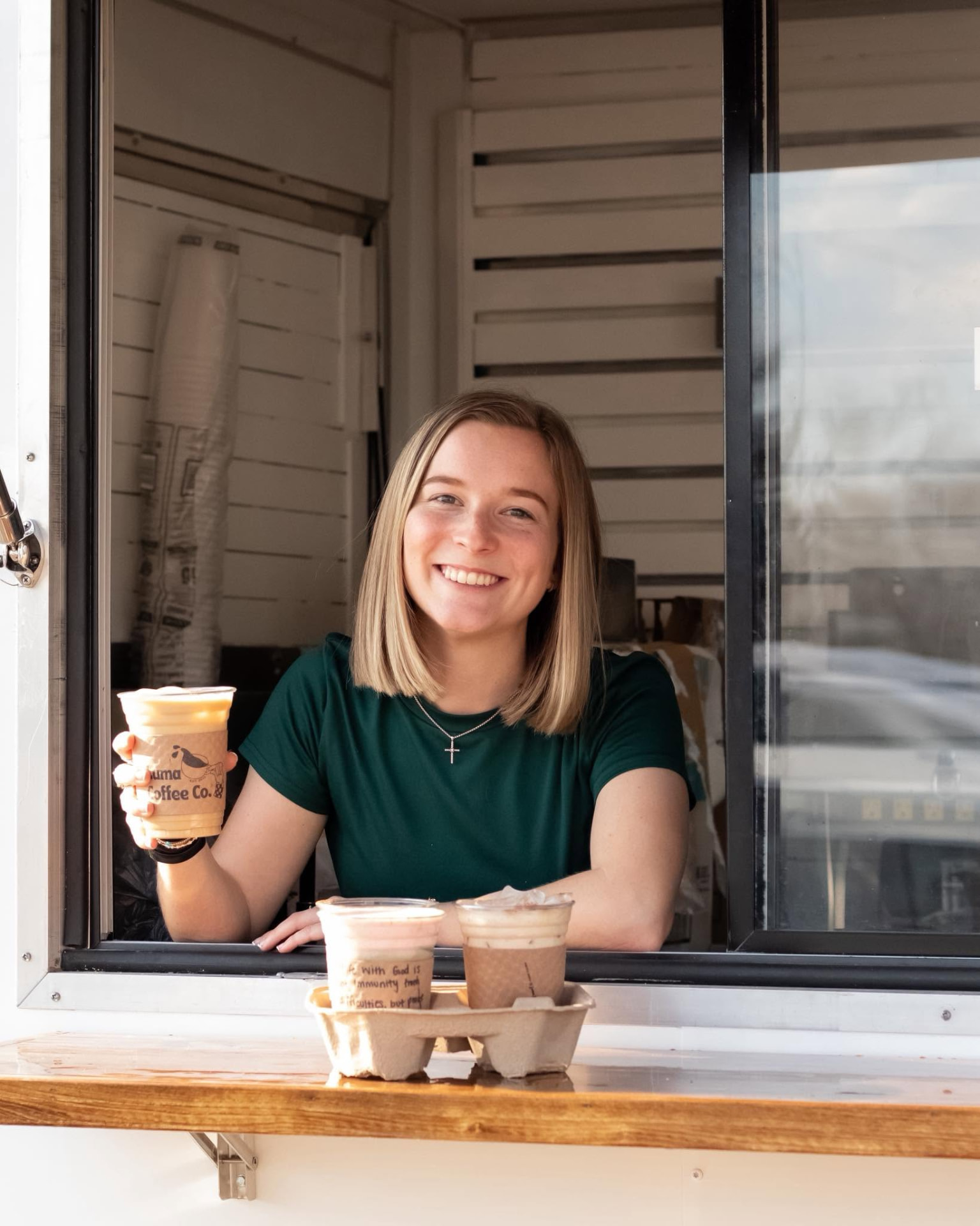 A friendly barista handing a drink out of the Luma Coffee Co. trailer window